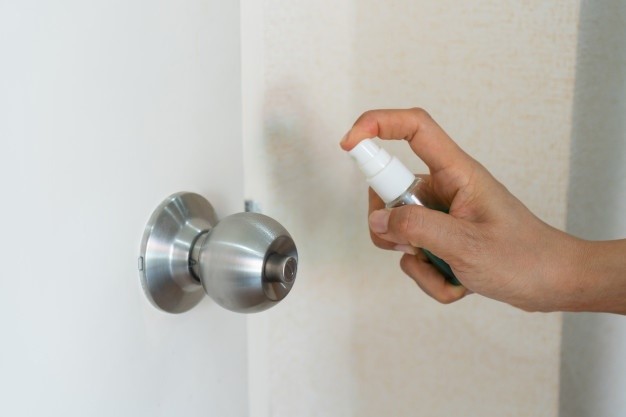 Woman spray alcohol to door knob for protection against infectious virus, bacteria and germs.